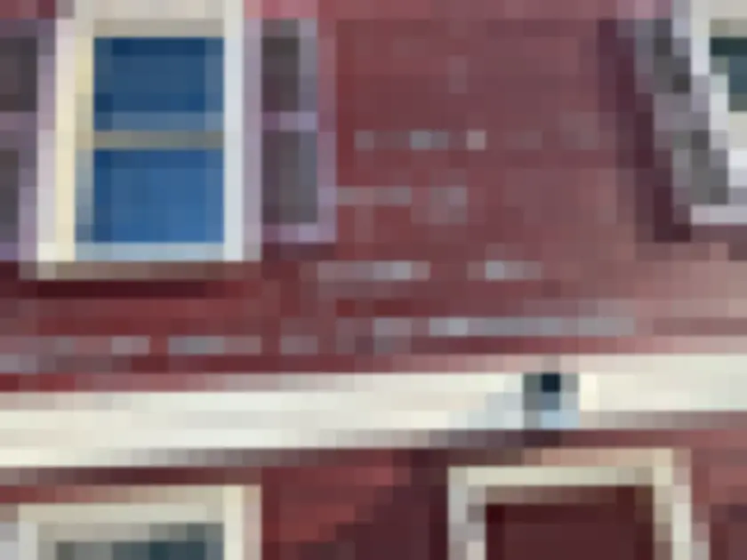 Photograph of exterior reddish painted wooden siding with widespread peeling paint around window